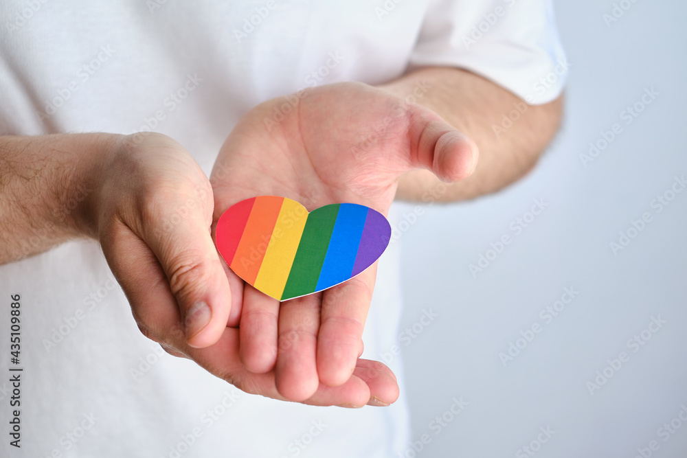 Rainbow heart from paper in man hands in white t-shirt. LGBT flag. LGBTQIA Pride Month in June. Lesbian Gay Bisexual Transgender. Gender equality. Human rights and tolerance. Rainbow flag