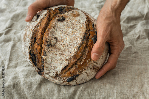 Fresh loaf of sourdough wholegrain spelt wheat bread in male hands. Natural linen fabric background. Buy local, support small business. Healthy traditional craft, hobby, baking at home. Copy space.