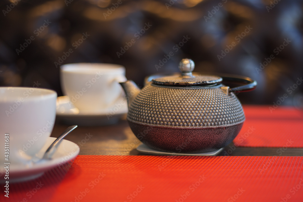 Teapot and pair of ceramic cups with five o'clock tea in a cafe. Lifestyle background. Close-up with shallow dof.