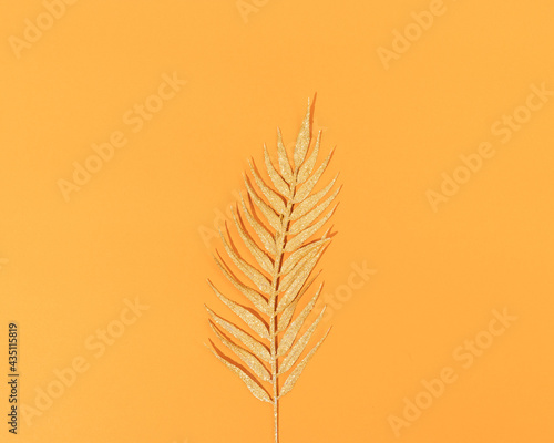 Shiny golden palm leaf on an orange background