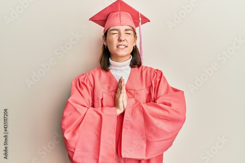 Young caucasian woman wearing graduation cap and ceremony robe begging and praying with hands together with hope expression on face very emotional and worried. begging.