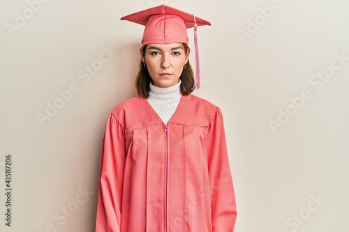 Young caucasian woman wearing graduation cap and ceremony robe relaxed with serious expression on face. simple and natural looking at the camera.
