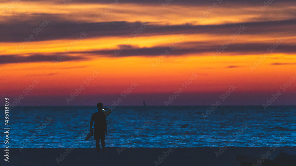 Man takes photo with phone on holiday at beach, silhouette sunset