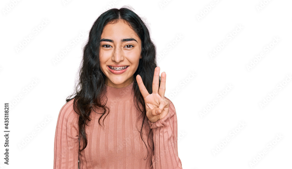 Hispanic teenager girl with dental braces wearing casual clothes showing and pointing up with fingers number three while smiling confident and happy. Hispanic teenager girl with dental braces wearing casual clothes showing and pointing up with fingers number three while smiling confident and happy.