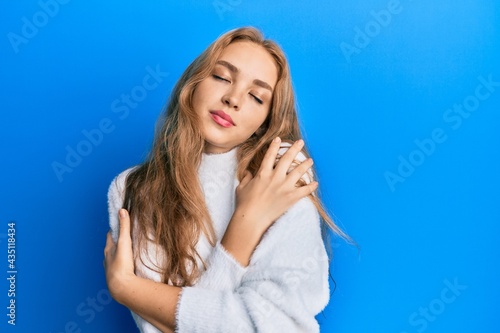 Beautiful blonde caucasian woman wearing casual winter sweater hugging oneself happy and positive, smiling confident. self love and self care