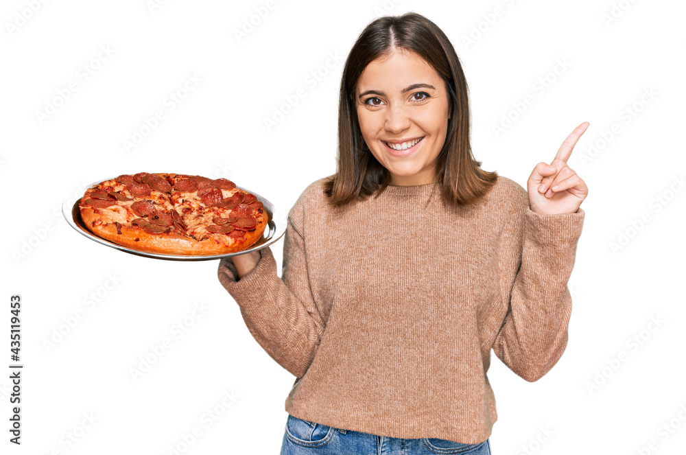 Young beautiful woman holding italian pizza surprised with an idea or question pointing finger with happy face, number one Young beautiful woman holding italian pizza surprised with an idea or question pointing finger with happy face, number one