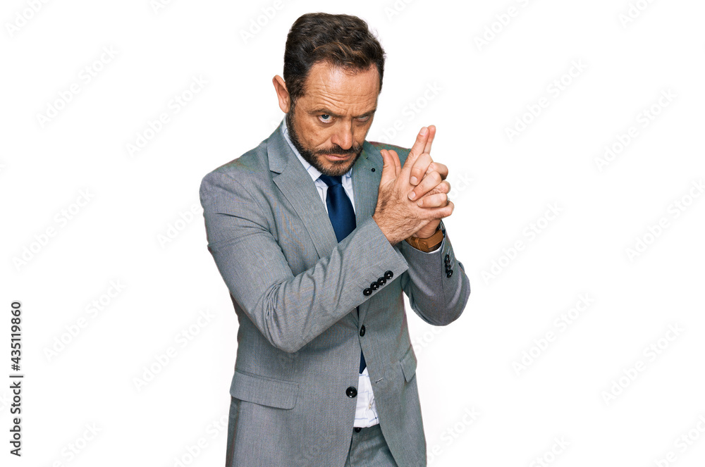 Middle age man wearing business clothes holding symbolic gun with hand gesture, playing killing shooting weapons, angry face Middle age man wearing business clothes holding symbolic gun with hand gesture, playing killing shooting weapons, angry face