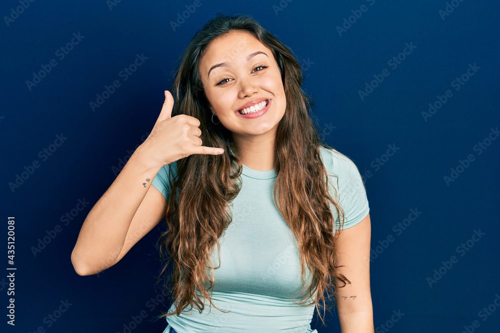 Young hispanic girl wearing casual clothes smiling doing phone gesture with hand and fingers like talking on the telephone. communicating concepts. Young hispanic girl wearing casual clothes smiling doing phone gesture with hand and fingers like talking on the telephone. communicating concepts.