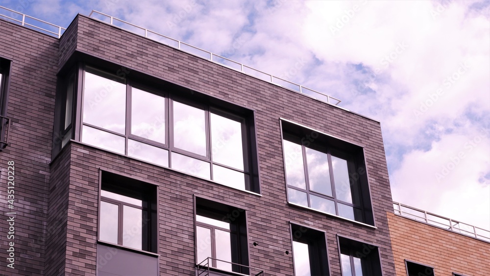 It is a modern brown brick building. Large windows reflecting the sky. Part of the building facade.
