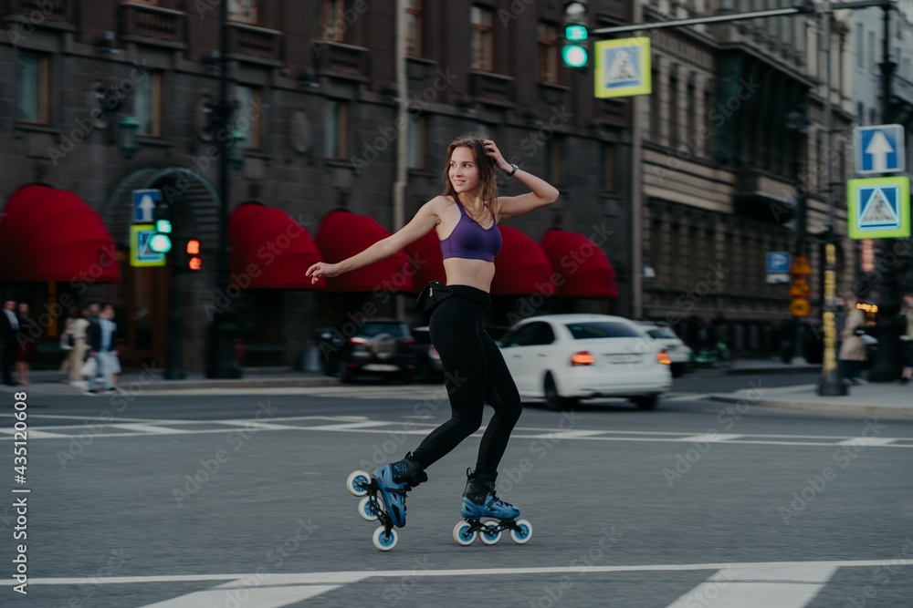 Outdoor shot of sim woman rides on rollerblades loks away trains different muscle groups of legs and core develops endurance manages her weight burns calories improves balancing. Cardio workout
