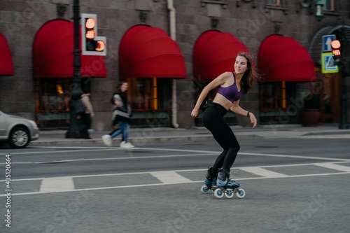 Slim sporty young woman uses rollerskates as mode of transportation in city enjoys favorite hobby ans boosts mood dressed in active wear poses on road exercises regularly keeps fit loses weight