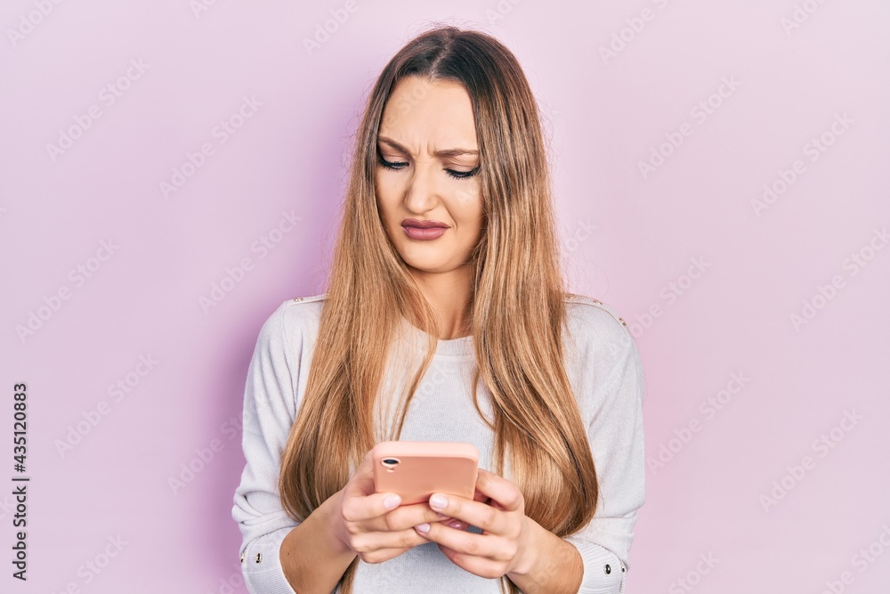 Young blonde girl using smartphone typing message clueless and confused expression. doubt concept. Young blonde girl using smartphone typing message clueless and confused expression. doubt concept.