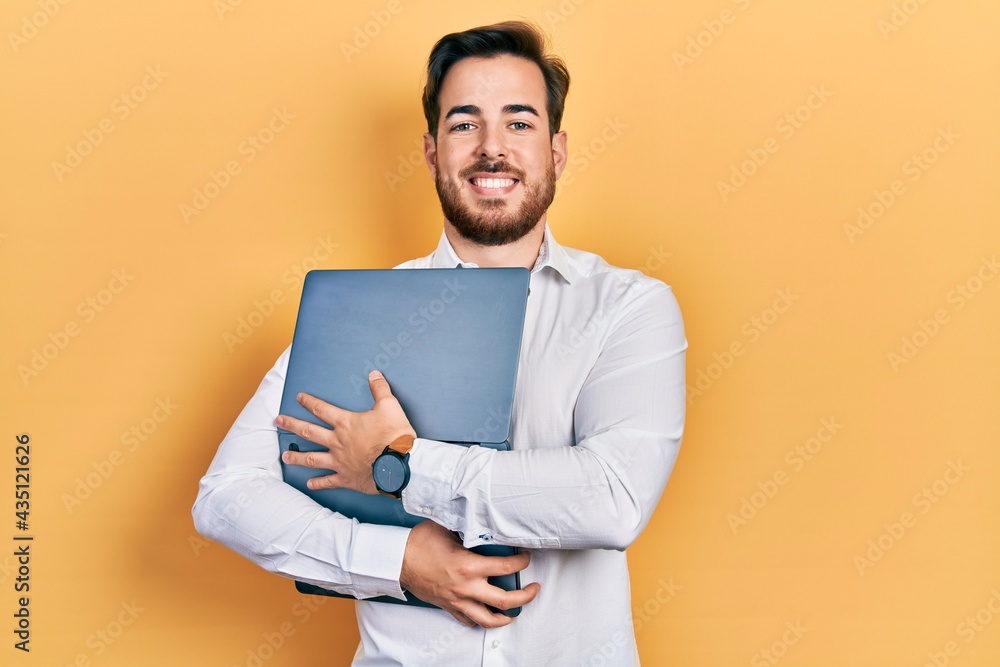 Handsome caucasian man with beard hugging laptop smiling with a happy and cool smile on face. showing teeth. Handsome caucasian man with beard hugging laptop smiling with a happy and cool smile on face. showing teeth.