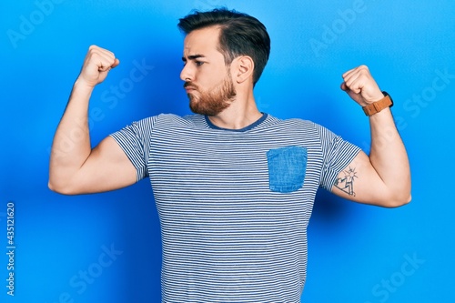 Handsome caucasian man with beard wearing casual striped t shirt showing arms muscles smiling proud. fitness concept.