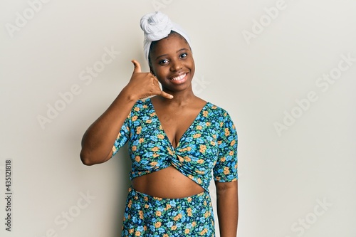 Young african woman wearing hair turban and african style smiling doing phone gesture with hand and fingers like talking on the telephone. communicating concepts.
