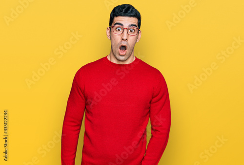Handsome hispanic man wearing casual clothes and glasses afraid and shocked with surprise expression, fear and excited face.