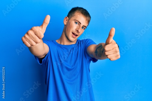 Young caucasian man wearing casual blue t shirt approving doing positive gesture with hand, thumbs up smiling and happy for success. winner gesture. © Krakenimages.com