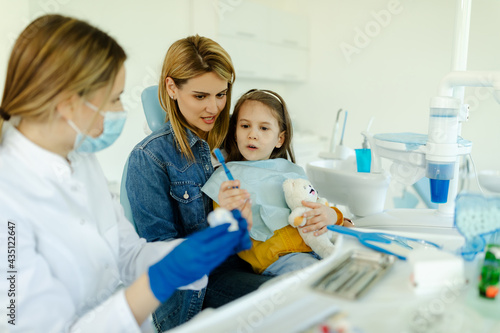 The girl is holding a toothbrush. A young doctor teaching a girl how to brush her teeth properly.