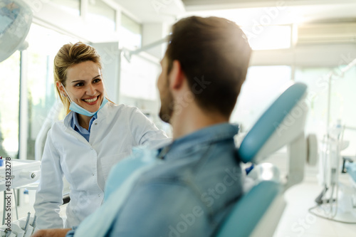 Beautiful female dentist talking with happy male patient at clinic.