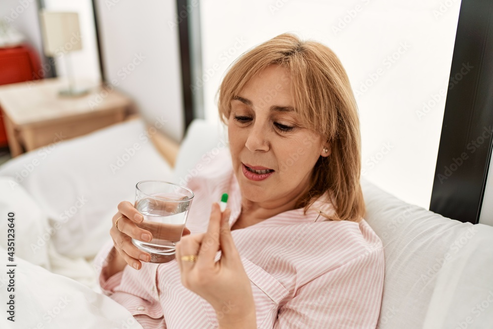 Middle age blonde woman illness taking pill lying on the bed at home.