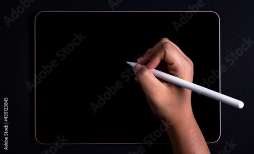 Brown hand using a pencil on a tablet