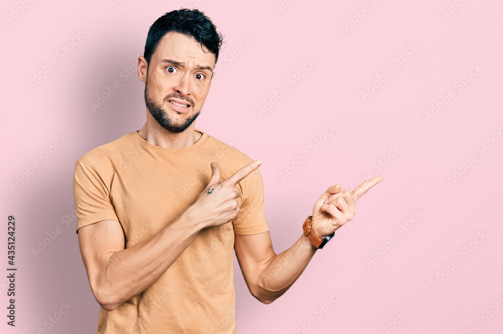 Hispanic man with beard wearing casual t shirt pointing aside worried and nervous with both hands, concerned and surprised expression