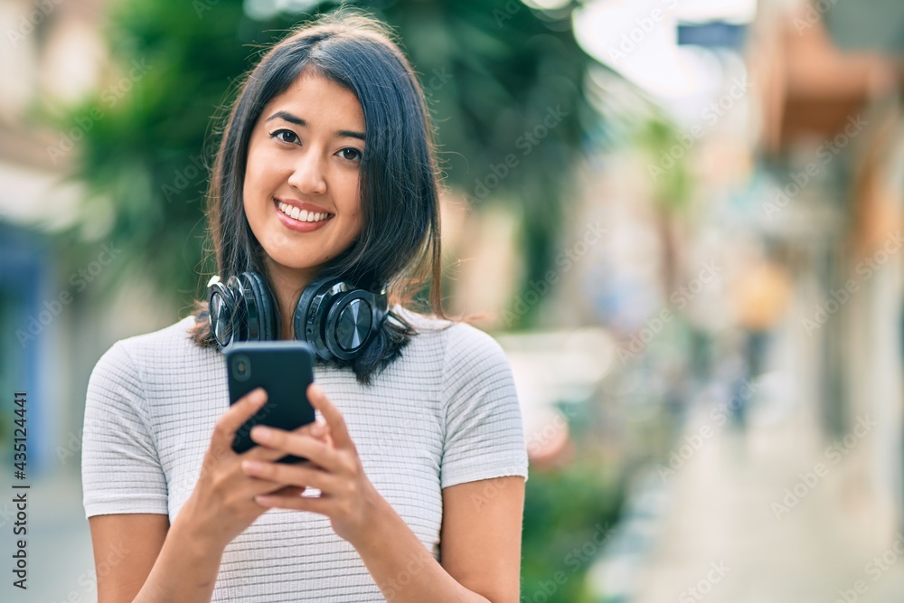 Young hispanic woman smiling happy using smartphone and headphones at the city.