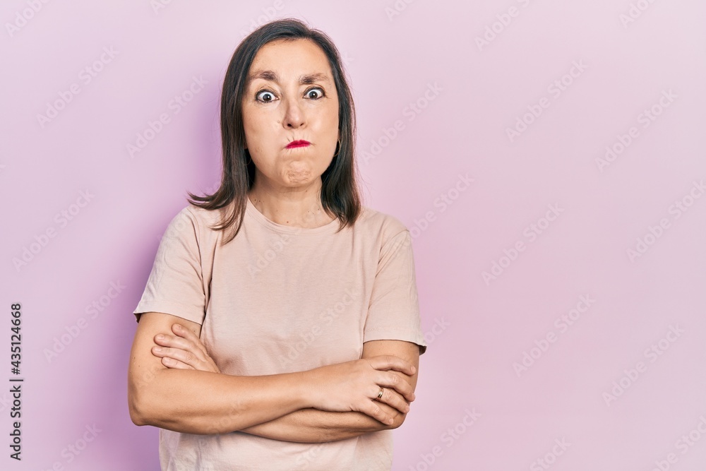 Obraz premium Middle age hispanic woman with arms crossed gesture puffing cheeks with funny face. mouth inflated with air, catching air.