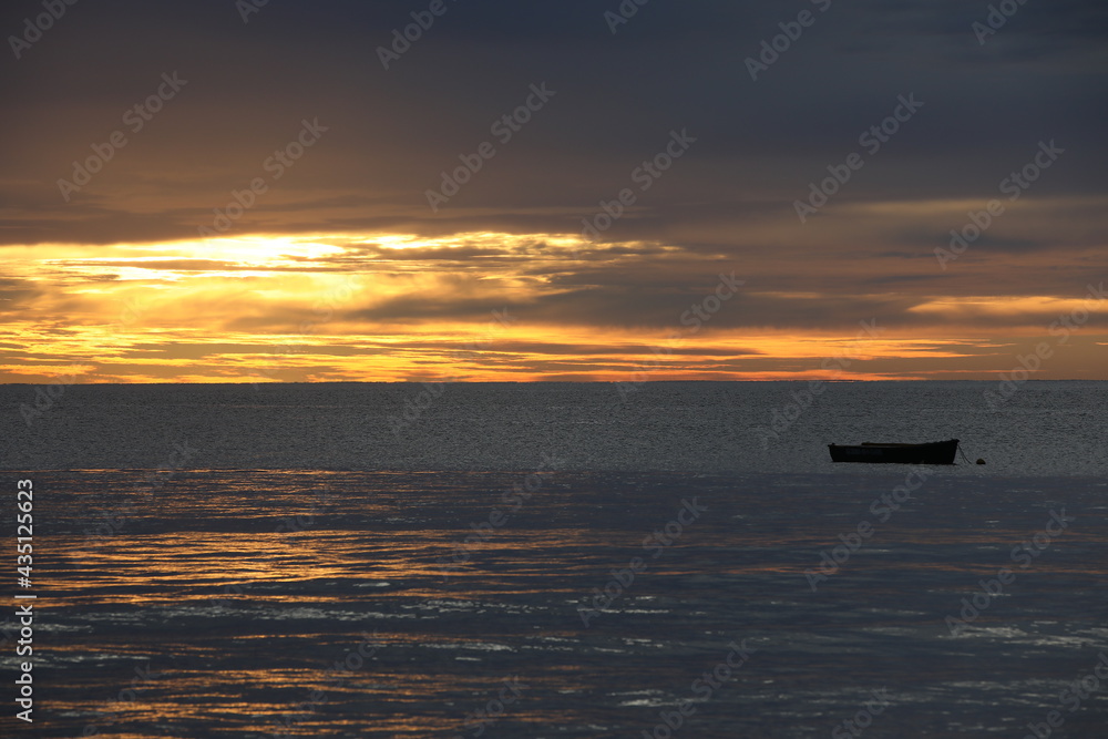 A lone fishing boat in the sea at sunset.A picturesque seascape with a burning orange sky on the horizon.End of the day at the equator.The concept of recreation travel and adventure A lone fishing boat in the sea at sunset.A picturesque seascape with a burning orange sky on the horizon.End of the day at the equator.The concept of recreation travel and adventure
