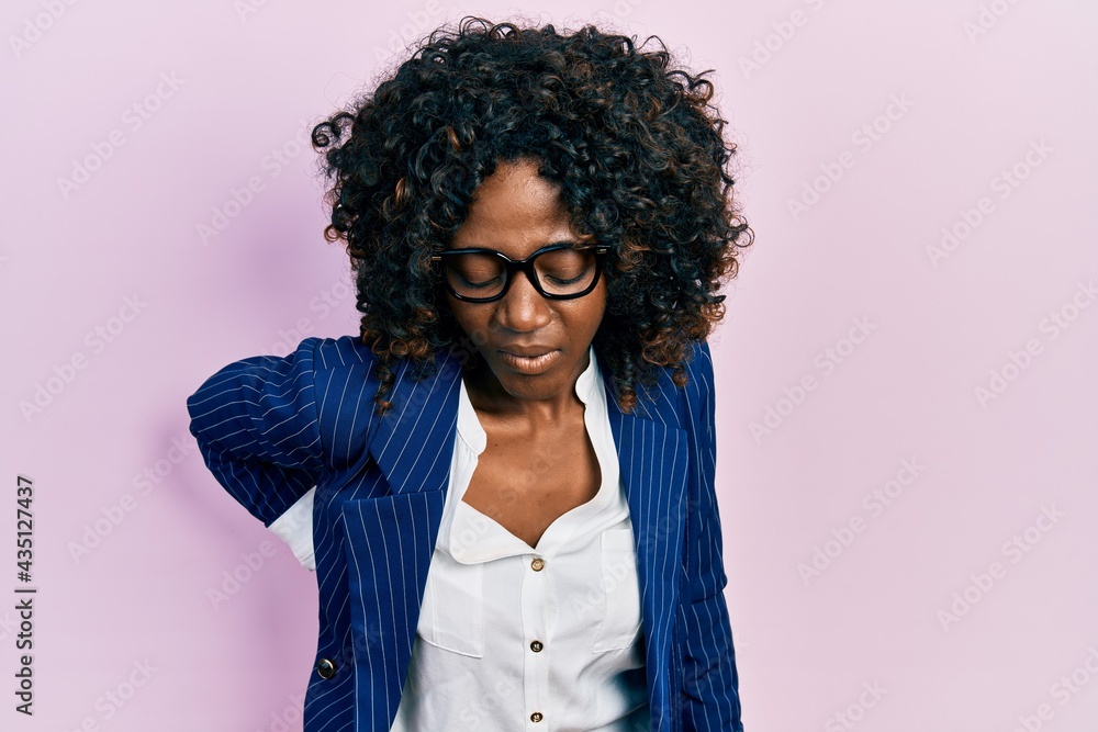 Young african american woman wearing business clothes and glasses suffering of backache, touching back with hand, muscular pain Young african american woman wearing business clothes and glasses suffering of backache, touching back with hand, muscular pain