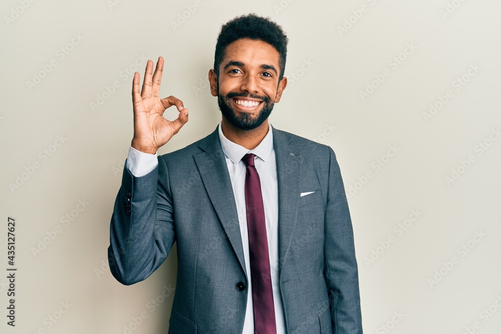 Handsome hispanic man with beard wearing business suit and tie smiling positive doing ok sign with hand and fingers. successful expression. Handsome hispanic man with beard wearing business suit and tie smiling positive doing ok sign with hand and fingers. successful expression.