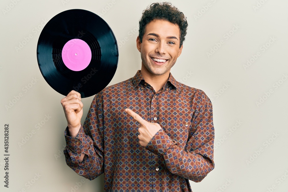 Young handsome man holding vinyl disc smiling happy pointing with hand and finger Young handsome man holding vinyl disc smiling happy pointing with hand and finger