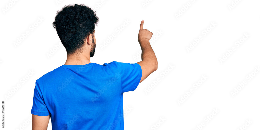 Young arab man with beard wearing casual blue t shirt posing backwards pointing ahead with finger hand Young arab man with beard wearing casual blue t shirt posing backwards pointing ahead with finger hand