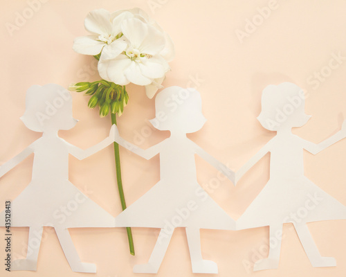 Row of paper doll girls holding stem of white fresh geranium; Paper doll friends holding hands on a soft peach background