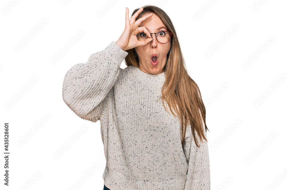 Young blonde woman wearing casual sweater and glasses doing ok gesture shocked with surprised face, eye looking through fingers. unbelieving expression.