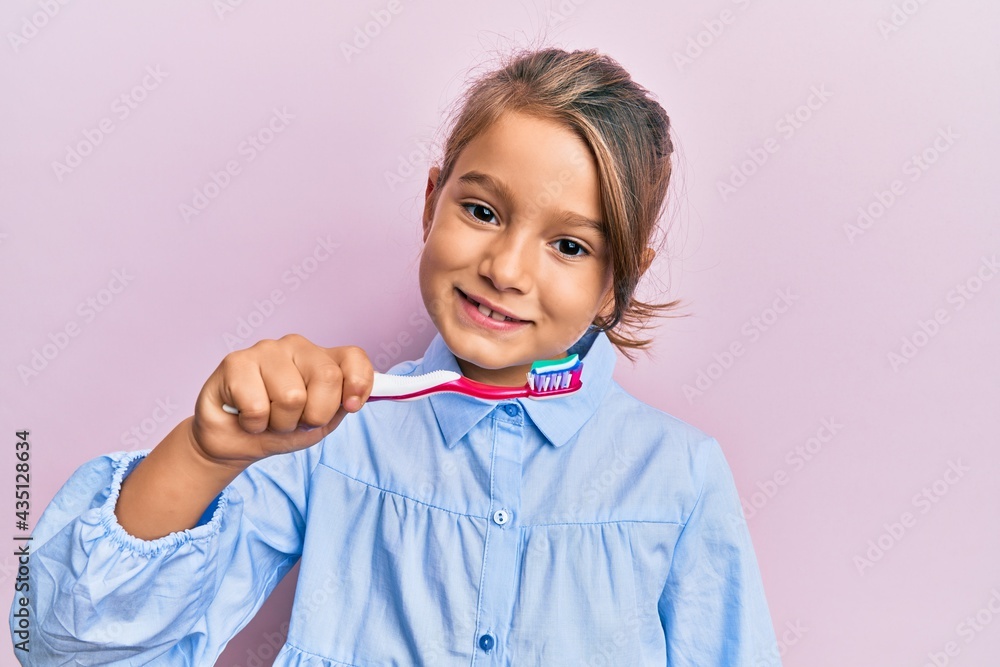 Little beautiful girl holding toothbrush with toothpaste looking positive and happy standing and smiling with a confident smile showing teeth Little beautiful girl holding toothbrush with toothpaste looking positive and happy standing and smiling with a confident smile showing teeth