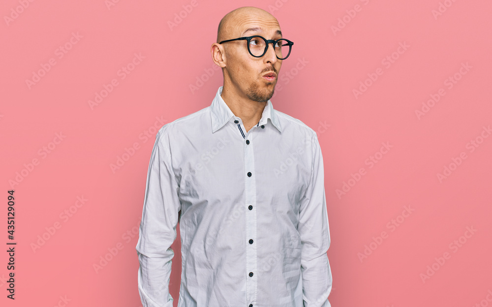 Bald man with beard wearing business shirt and glasses smiling looking to the side and staring away thinking.