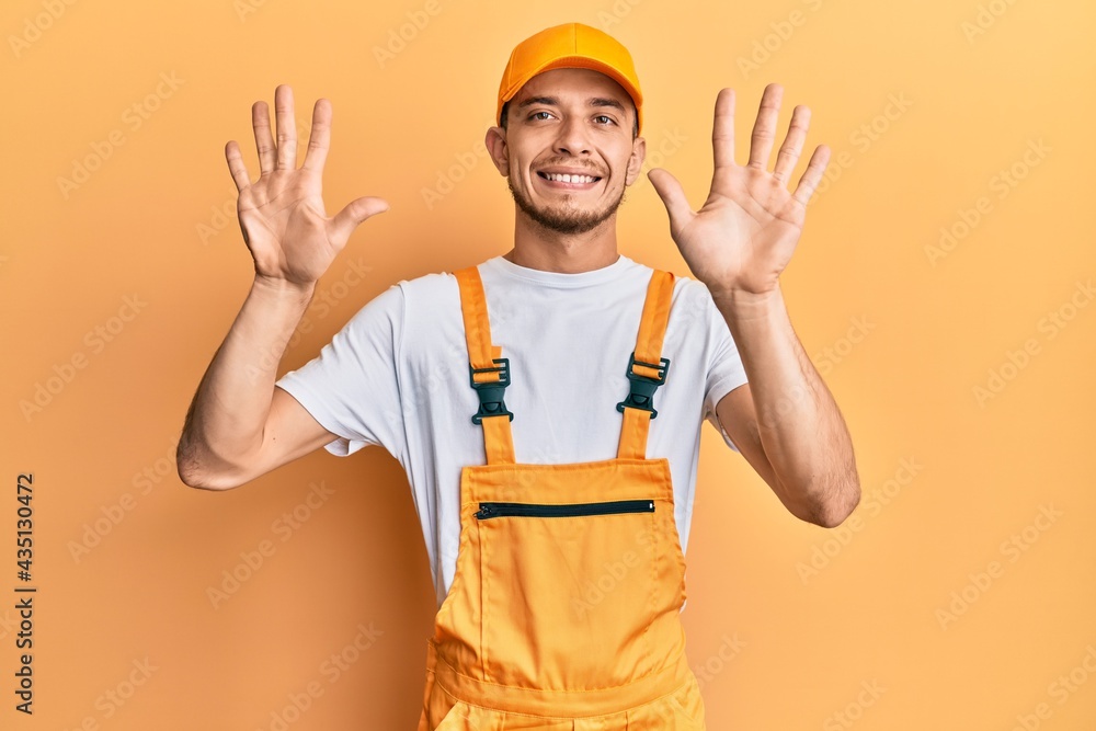 Hispanic young man wearing handyman uniform showing and pointing up with fingers number ten while smiling confident and happy. Hispanic young man wearing handyman uniform showing and pointing up with fingers number ten while smiling confident and happy.