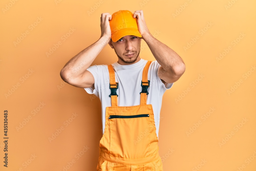 Hispanic young man wearing handyman uniform suffering from headache desperate and stressed because pain and migraine. hands on head.