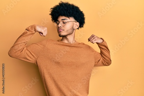 Young african american man with afro hair wearing casual winter sweater showing arms muscles smiling proud. fitness concept.