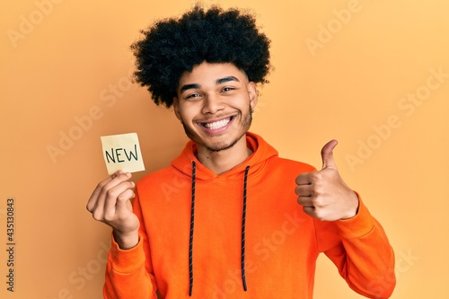 Young african american man with afro hair holding new word on paper smiling happy and positive, thumb up doing excellent and approval sign