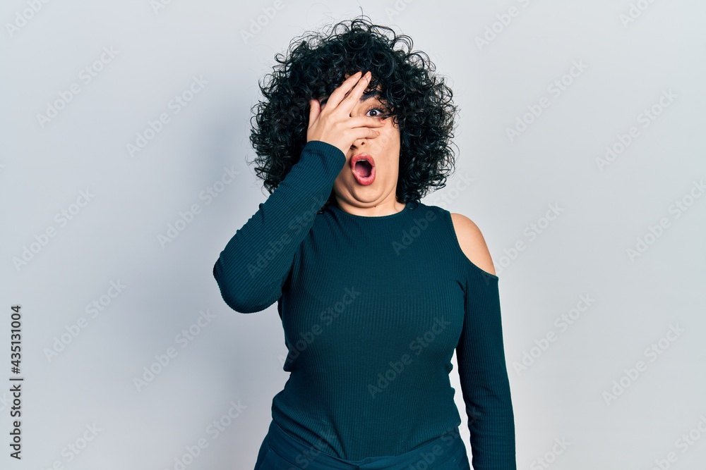Young middle east woman wearing casual clothes peeking in shock covering face and eyes with hand, looking through fingers afraid Young middle east woman wearing casual clothes peeking in shock covering face and eyes with hand, looking through fingers afraid