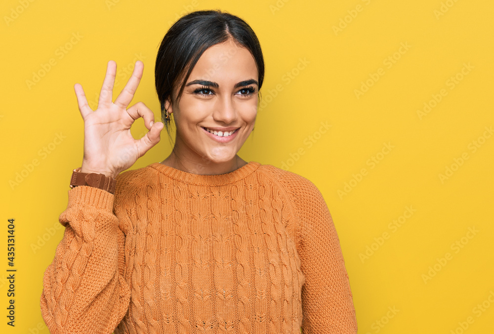 Young brunette woman wearing casual winter sweater smiling positive doing ok sign with hand and fingers. successful expression. Young brunette woman wearing casual winter sweater smiling positive doing ok sign with hand and fingers. successful expression.