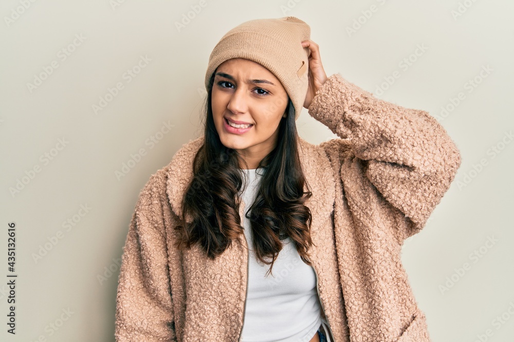 Young hispanic woman wearing wool sweater and winter hat confuse and wonder about question. uncertain with doubt, thinking with hand on head. pensive concept. Young hispanic woman wearing wool sweater and winter hat confuse and wonder about question. uncertain with doubt, thinking with hand on head. pensive concept.