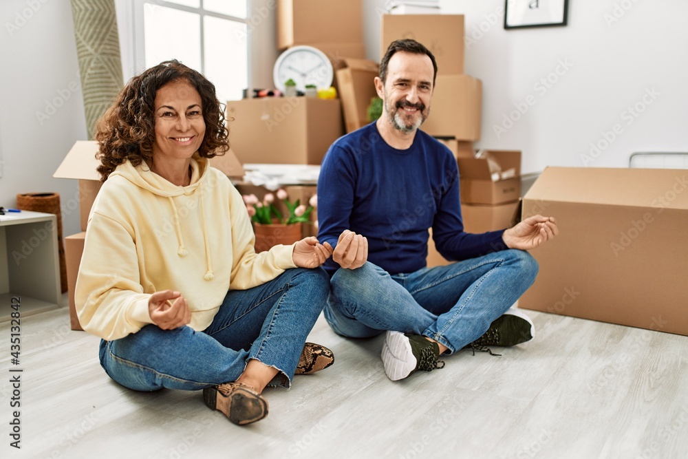 Middle age hispanic couple smiling happy sitting on the floor doing yoga pose new home. Middle age hispanic couple smiling happy sitting on the floor doing yoga pose new home.