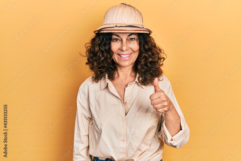 Middle age hispanic woman wearing explorer hat smiling happy and positive, thumb up doing excellent and approval sign Middle age hispanic woman wearing explorer hat smiling happy and positive, thumb up doing excellent and approval sign