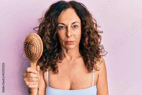 Middle age hispanic woman using comb thinking attitude and sober expression looking self confident