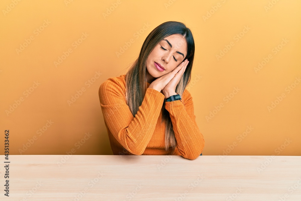 Young hispanic woman wearing casual clothes sitting on the table sleeping tired dreaming and posing with hands together while smiling with closed eyes. Young hispanic woman wearing casual clothes sitting on the table sleeping tired dreaming and posing with hands together while smiling with closed eyes.