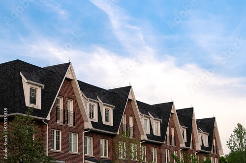 A row of new townhouses with peaked roofs against the blue sky. 