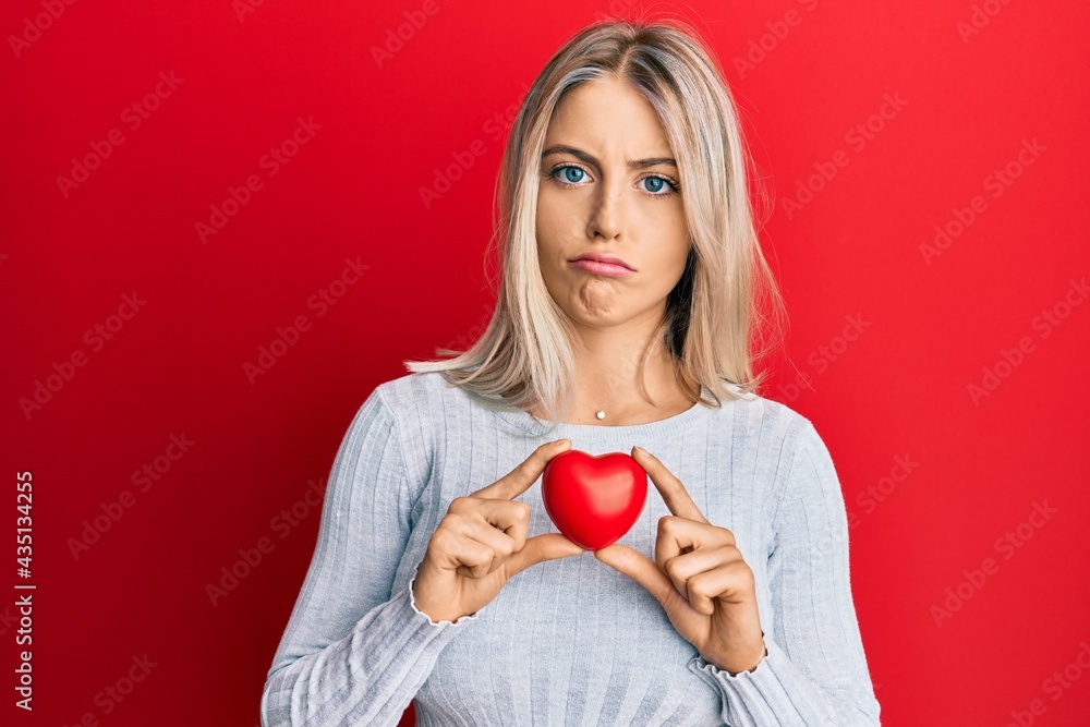 Beautiful blonde woman holding heart depressed and worry for distress, crying angry and afraid. sad expression. Beautiful blonde woman holding heart depressed and worry for distress, crying angry and afraid. sad expression.
